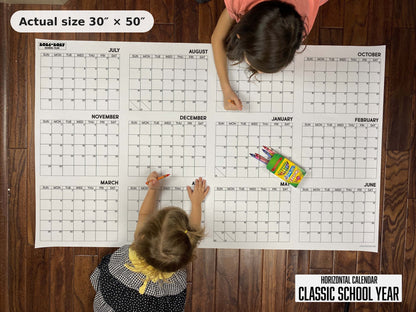 Two kids writing on the Classic School Year giant calendar on the floor, showing its real 30 x 50 inch size