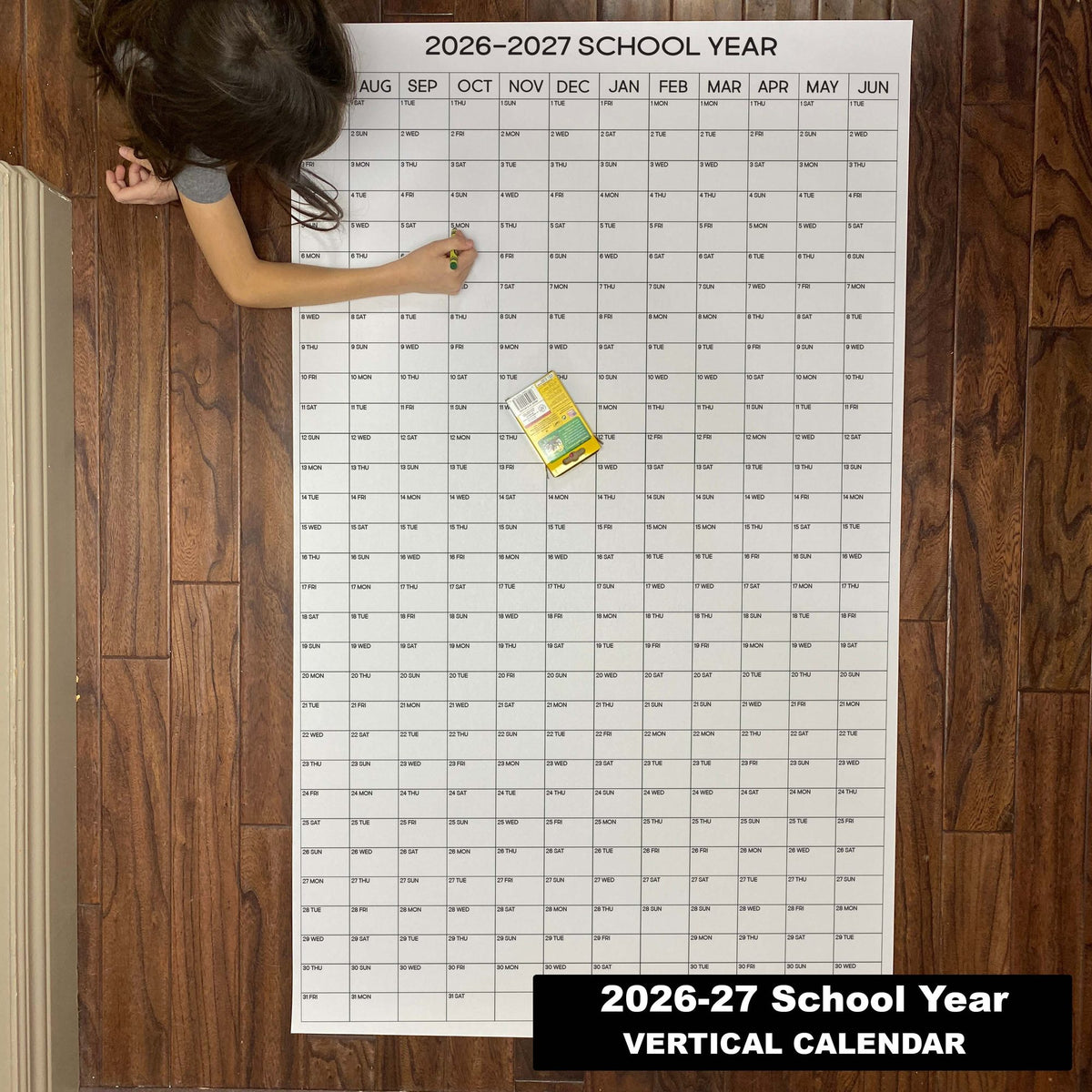Child writing on the 2026-27 School Year vertical giant paper wall calendar on a wood floor