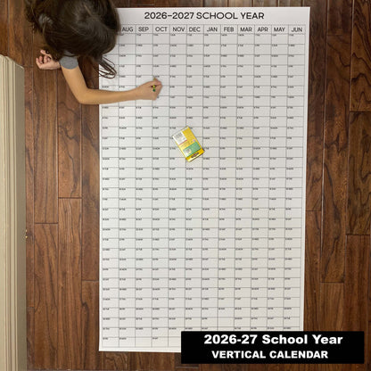 Child writing on the 2026-27 School Year vertical giant paper wall calendar on a wood floor