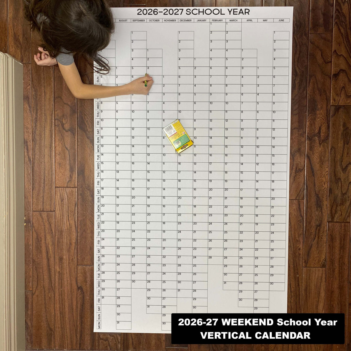 Child writing on the 2026-27 weekend-aligned vertical school year giant paper wall calendar on a wood floor