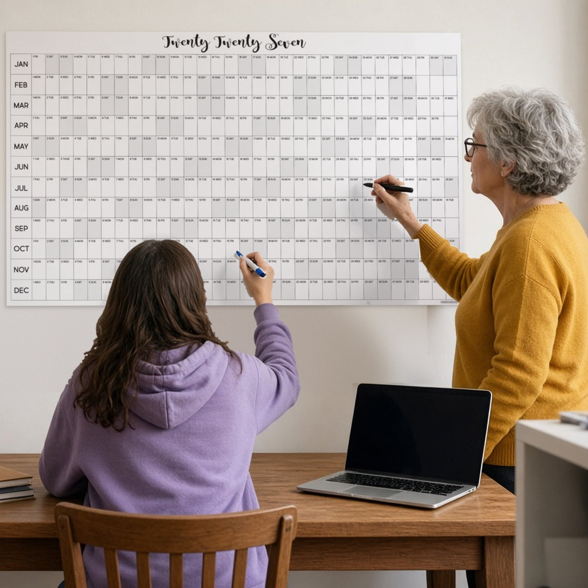Grandmother and teen writing plans on the giant 2027 yearly wall calendar in a home office