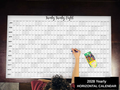 Child writing on the 2028 yearly horizontal giant paper wall calendar on a wood floor