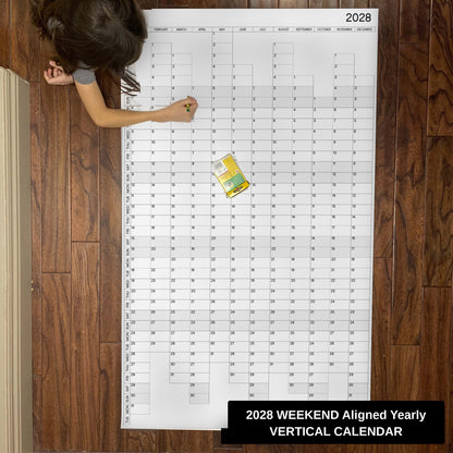 Child writing on the 2028 weekend-aligned yearly vertical giant paper wall calendar on a wood floor