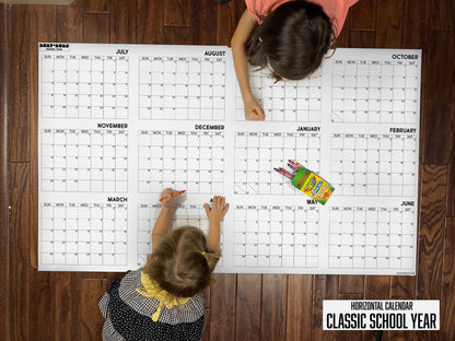 Child writing on the 2027-28 Classic School Year horizontal giant paper wall calendar on a wood floor