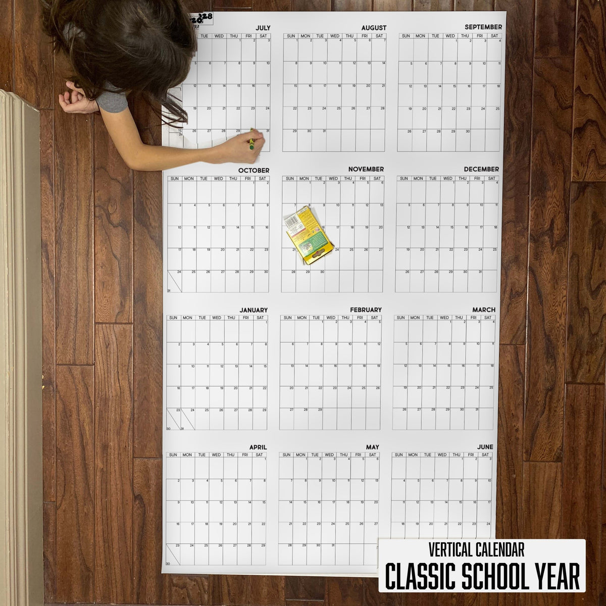 Child writing on the 2027-28 Classic School Year vertical giant paper wall calendar on a wood floor