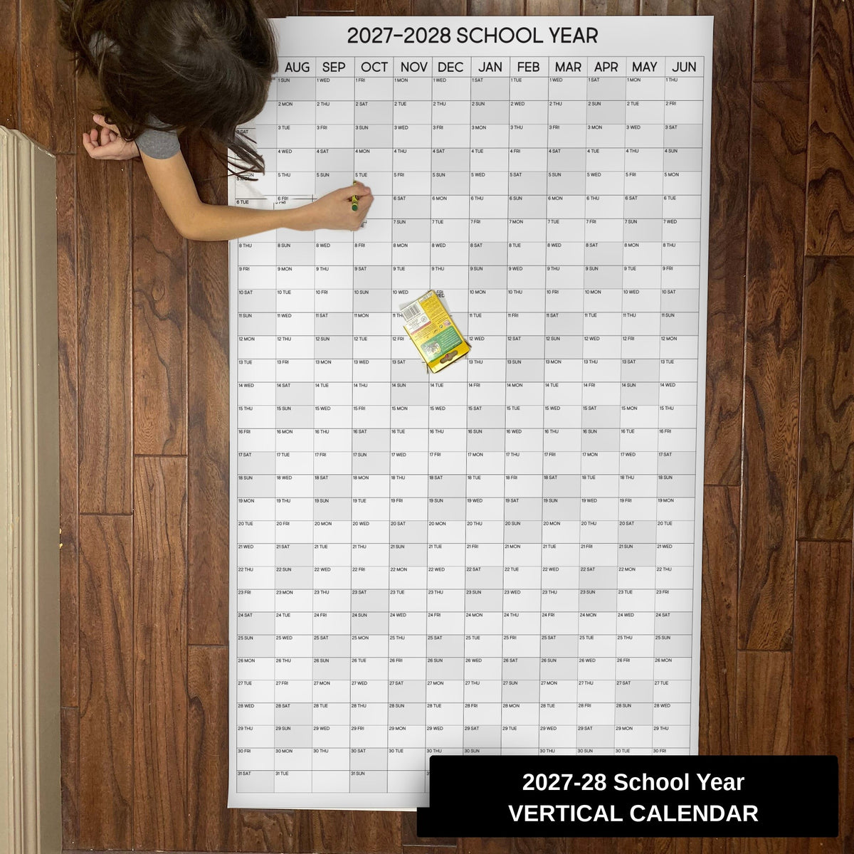 Child writing on the 2027-28 School Year vertical giant paper wall calendar on a wood floor