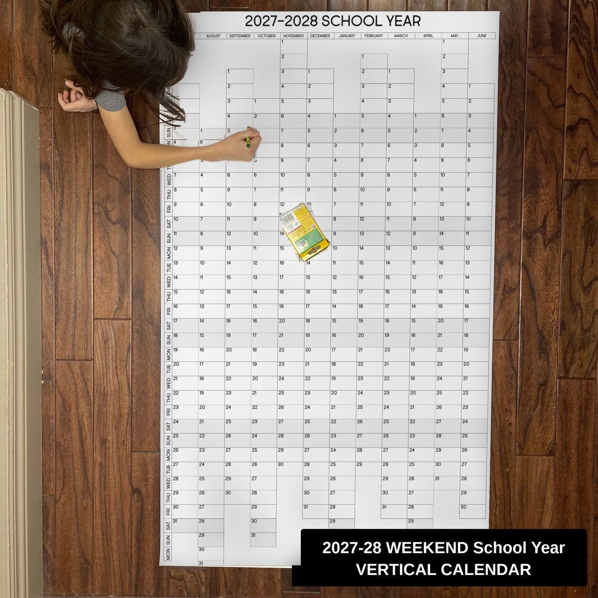 Child writing on the 2027-28 weekend-aligned vertical school year giant paper wall calendar on a wood floor