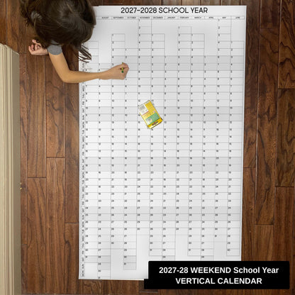 Child writing on the 2027-28 weekend-aligned vertical school year giant paper wall calendar on a wood floor