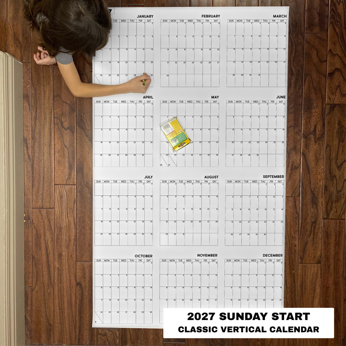 Child coloring the 2027 Sunday start classic vertical yearly calendar on the floor