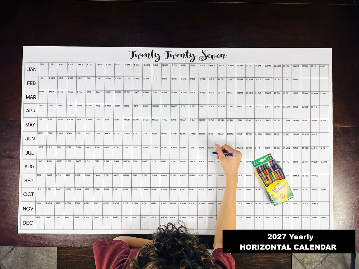 Child writing on the 2027 yearly horizontal giant paper wall calendar on a wood floor
