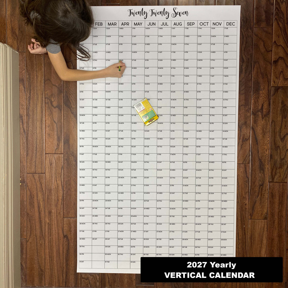 Child writing on the 2027 yearly vertical giant paper wall calendar on a wood floor