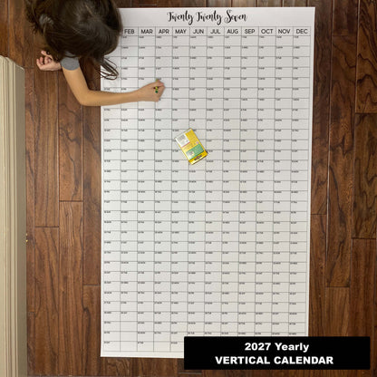 Child writing on the 2027 yearly vertical giant paper wall calendar on a wood floor