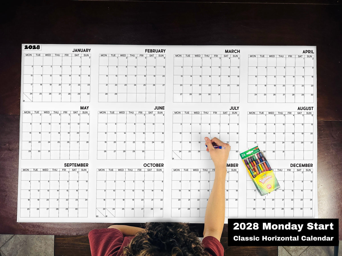 Child coloring the 2028 Monday start classic horizontal yearly calendar on a table