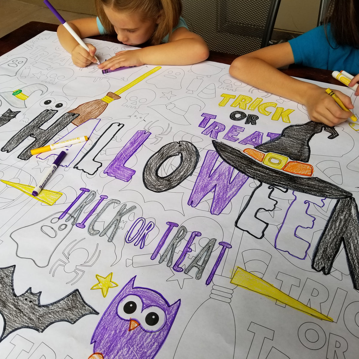 The Happy Halloween giant coloring sheet being colored in with markers at a table