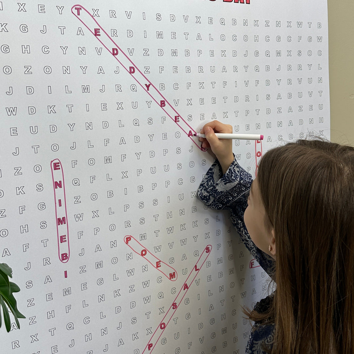 Kids circling words on the Valentines Day giant word search hung on a wall
