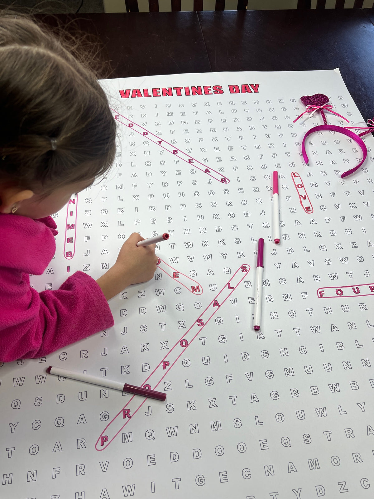 Kids circling words on the Valentines Day giant word search hung on a wall