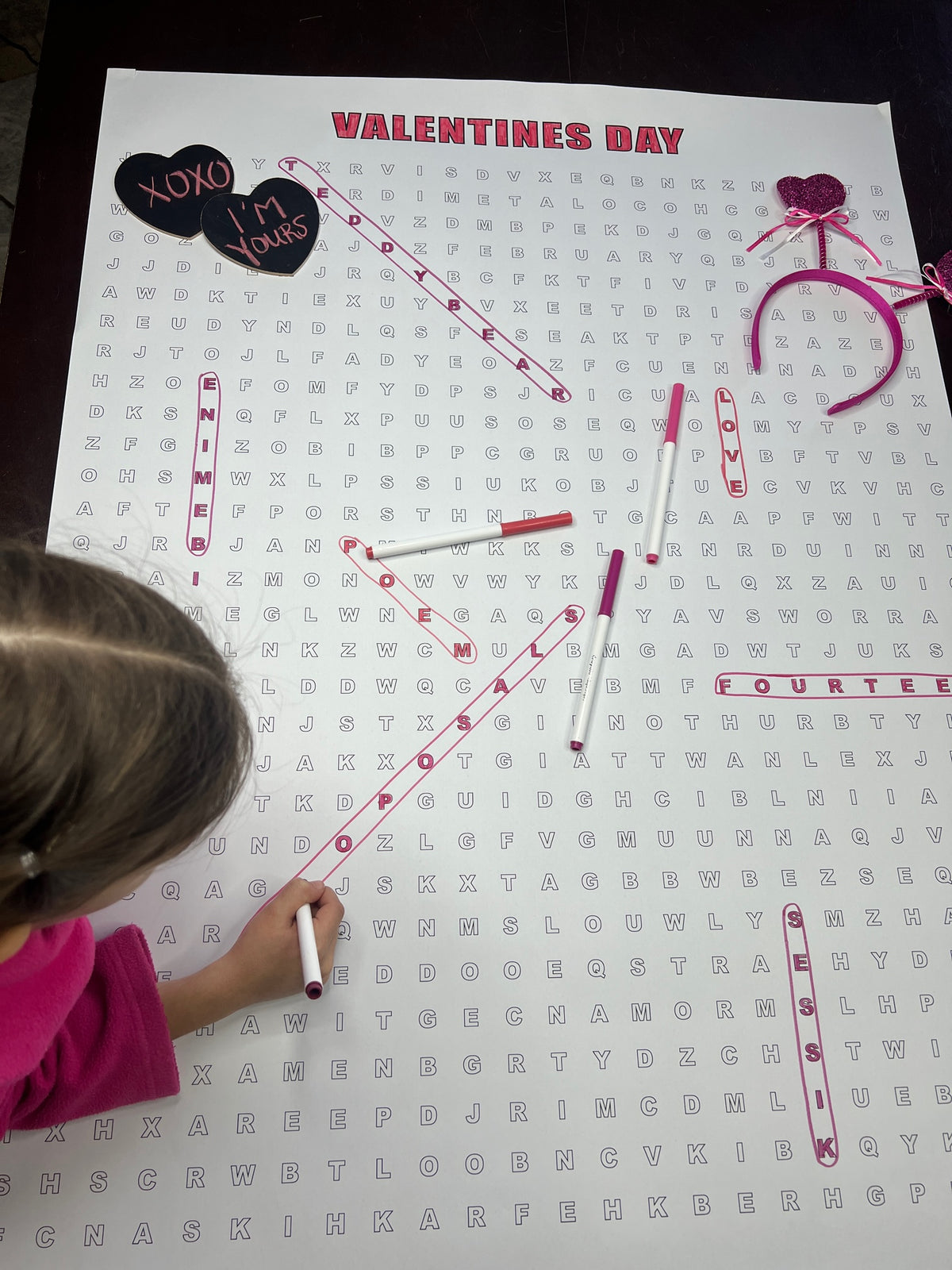 Kids circling words on the Valentines Day giant word search hung on a wall