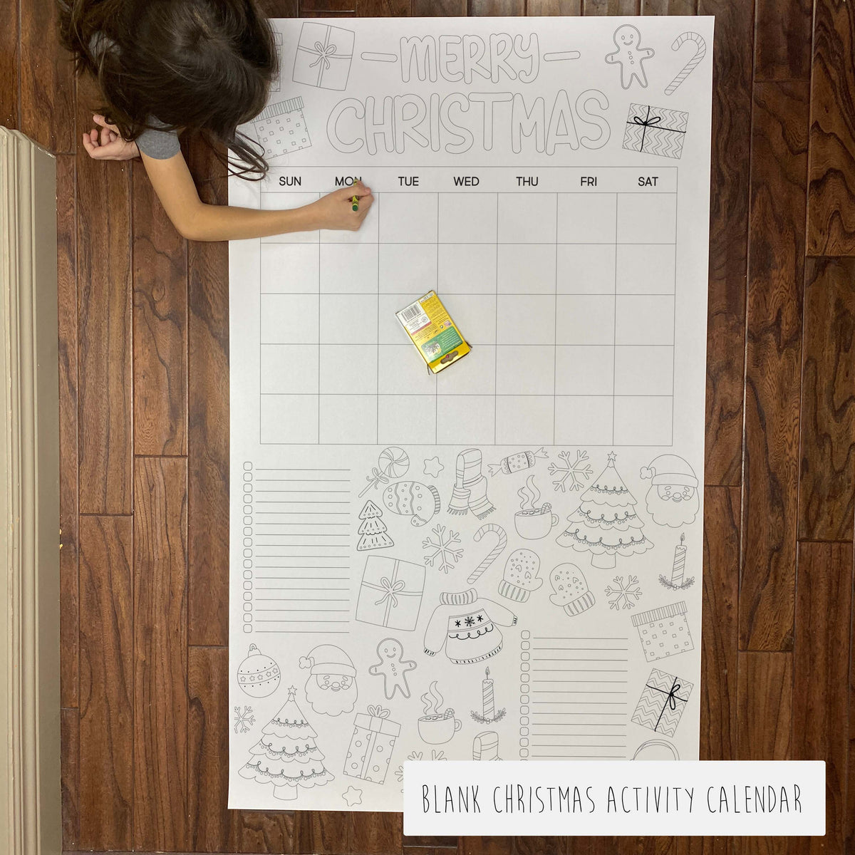 Blank Christmas activity calendar on a wooden floor with a child's hand holding it.