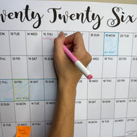 Thumbnail for Hand holding a pink pen over a calendar with 'Twenty Twenty Six' text.