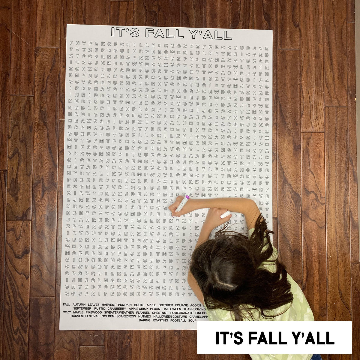 Child solving the It's Fall Y'all giant word search poster on a wood floor
