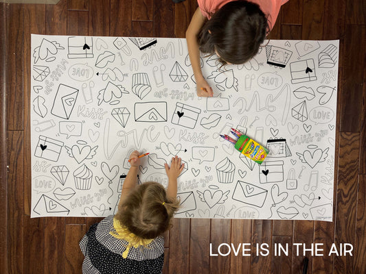 Child coloring the Love Is In The Air giant coloring sheet on a wood floor with crayons