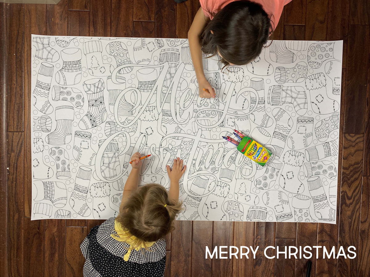 Child coloring the Merry Christmas giant coloring sheet on a wood floor with crayons