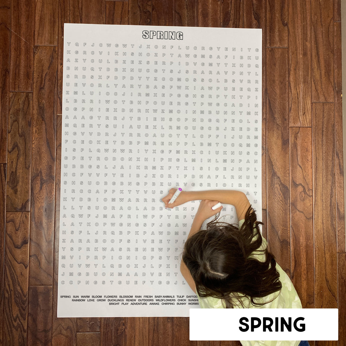 Child solving the Spring giant word search poster on a wood floor