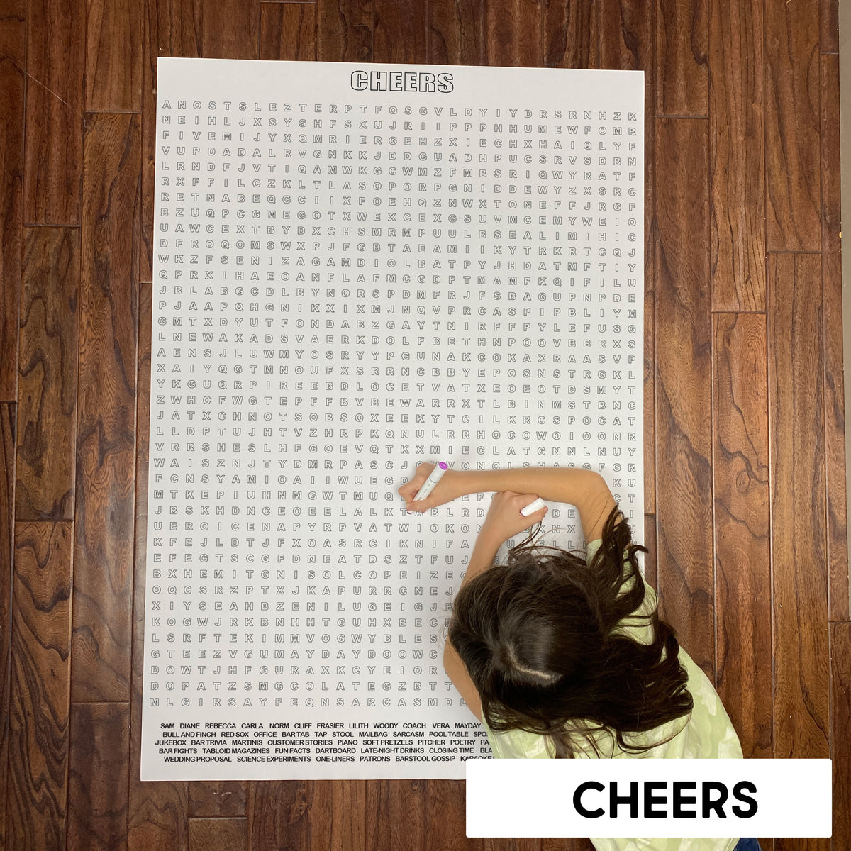Child solving a classic TV sitcom themed giant word search poster on a wood floor