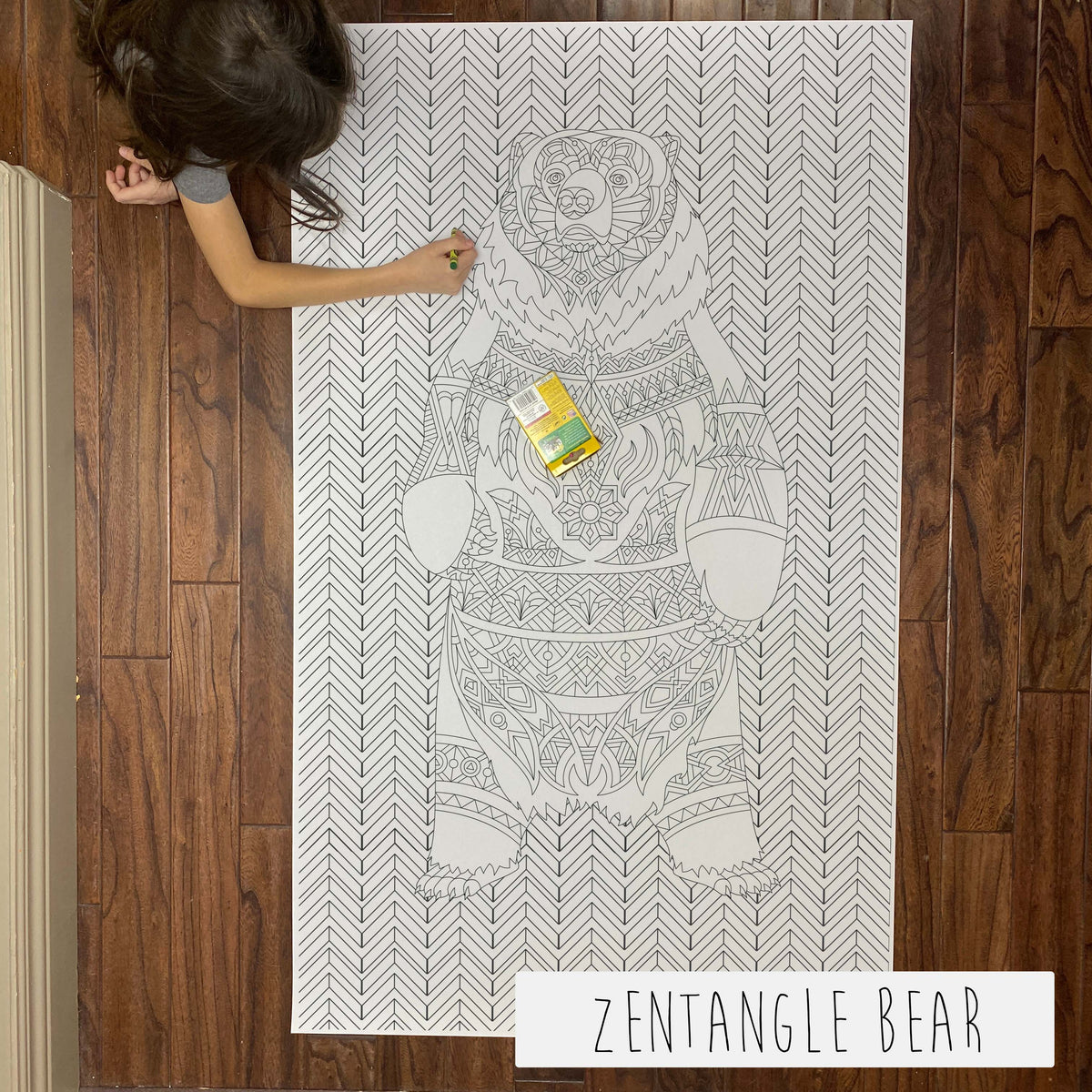 Child coloring the Zentangle Bear giant coloring sheet on a wood floor with crayons