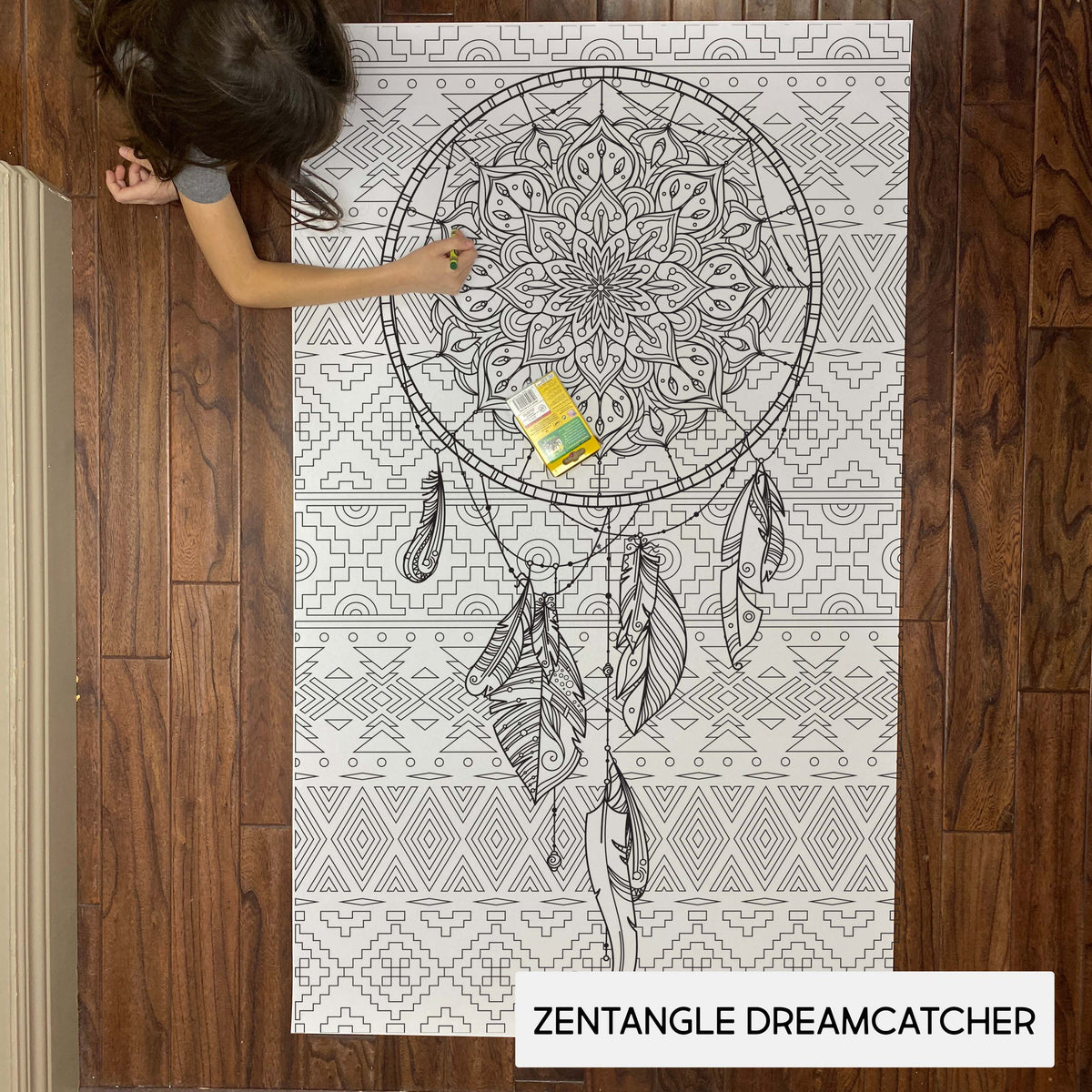 Child coloring the Zentangle Dreamcatcher giant coloring sheet on a wood floor with crayons