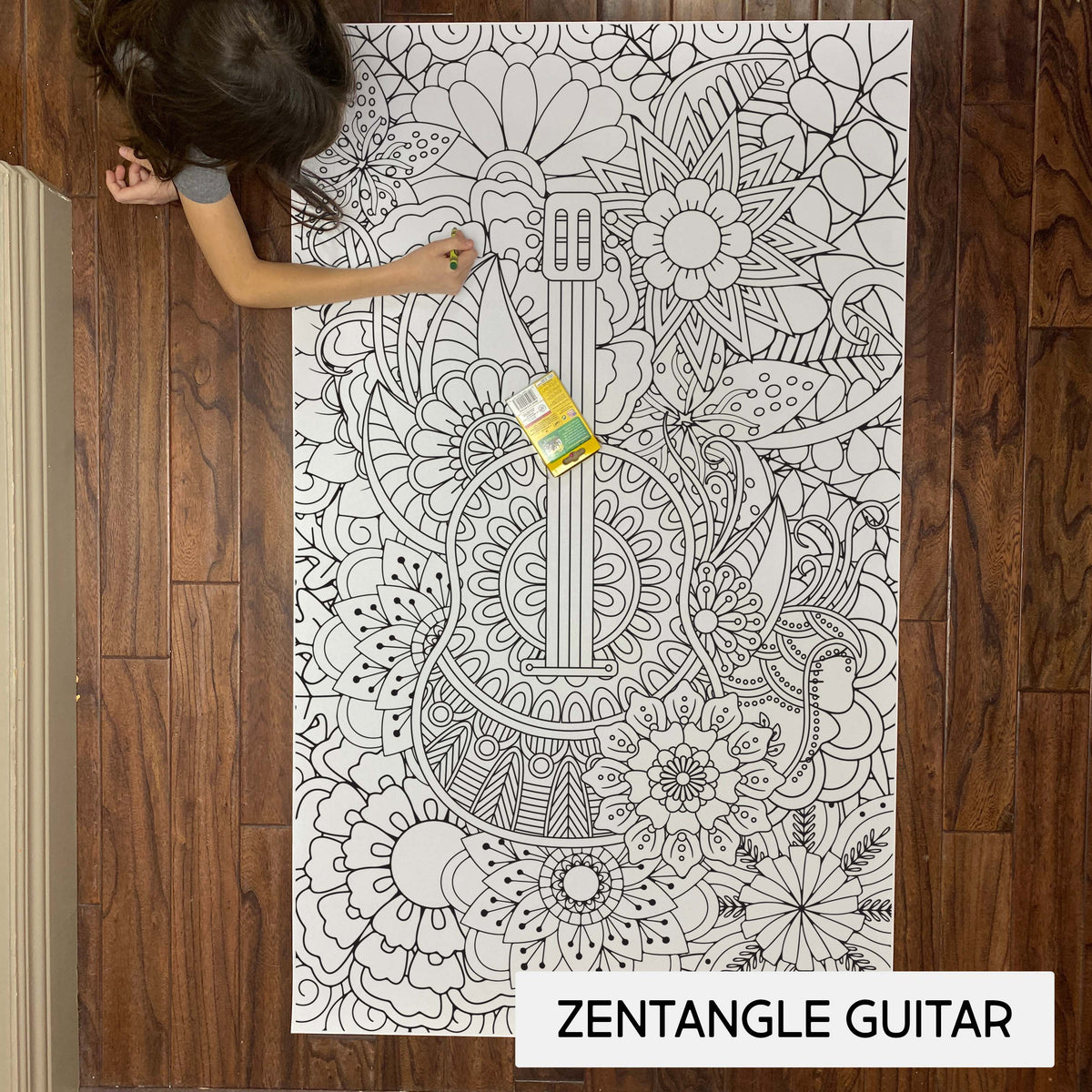 Child coloring the Zentangle Guitar giant coloring sheet on a wood floor with crayons