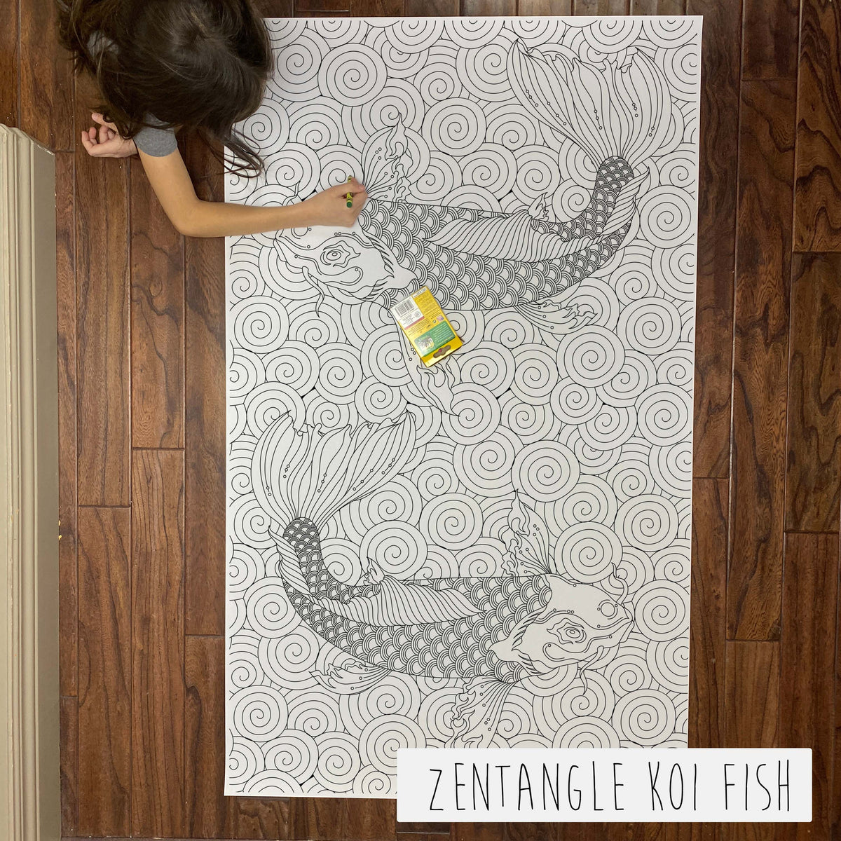 Child coloring the Zentangle Koi Fish giant coloring sheet on a wood floor with crayons
