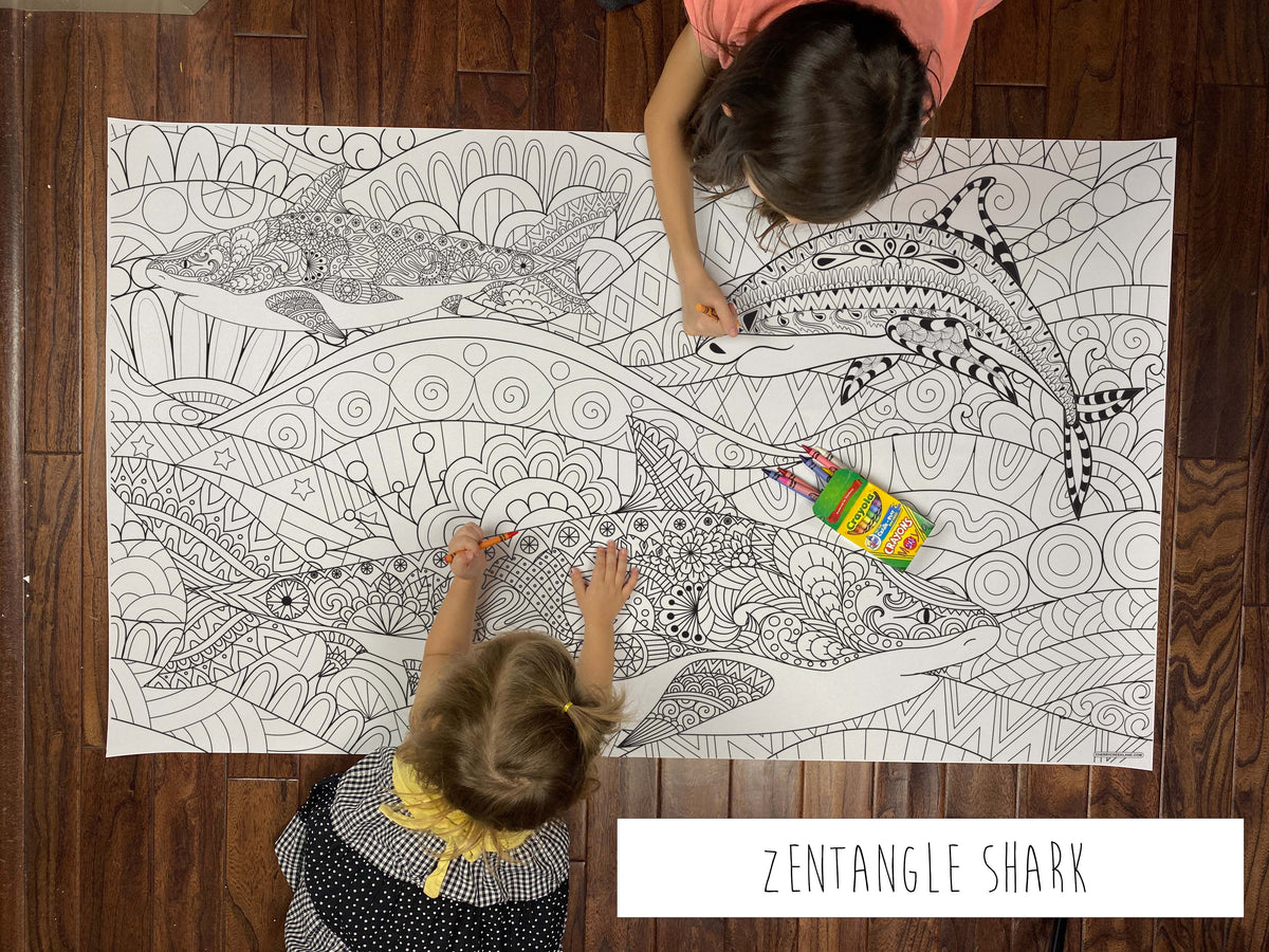 Child coloring the Zentangle Shark giant coloring sheet on a wood floor with crayons
