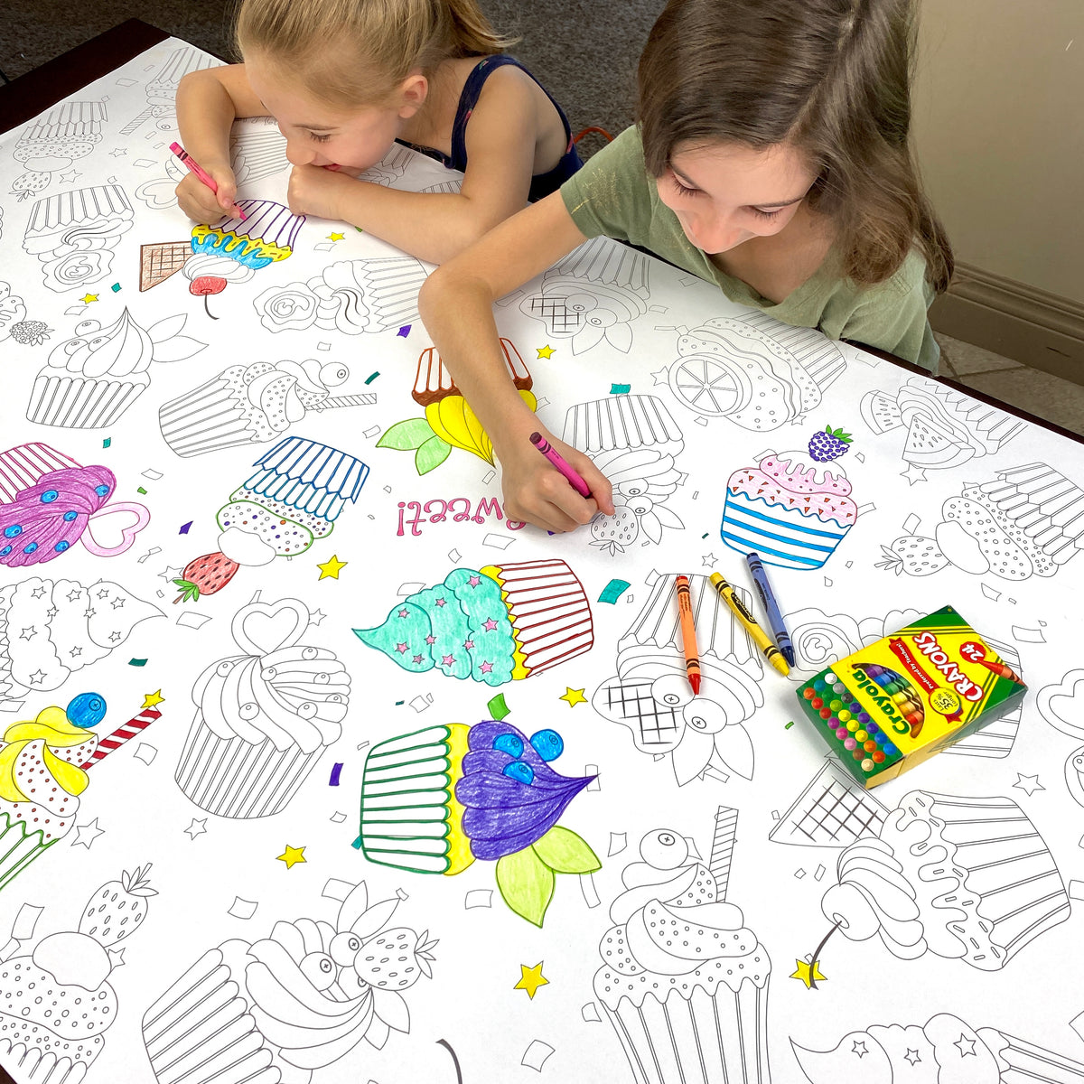 The Cupcakes giant coloring sheet being colored in with markers at a table