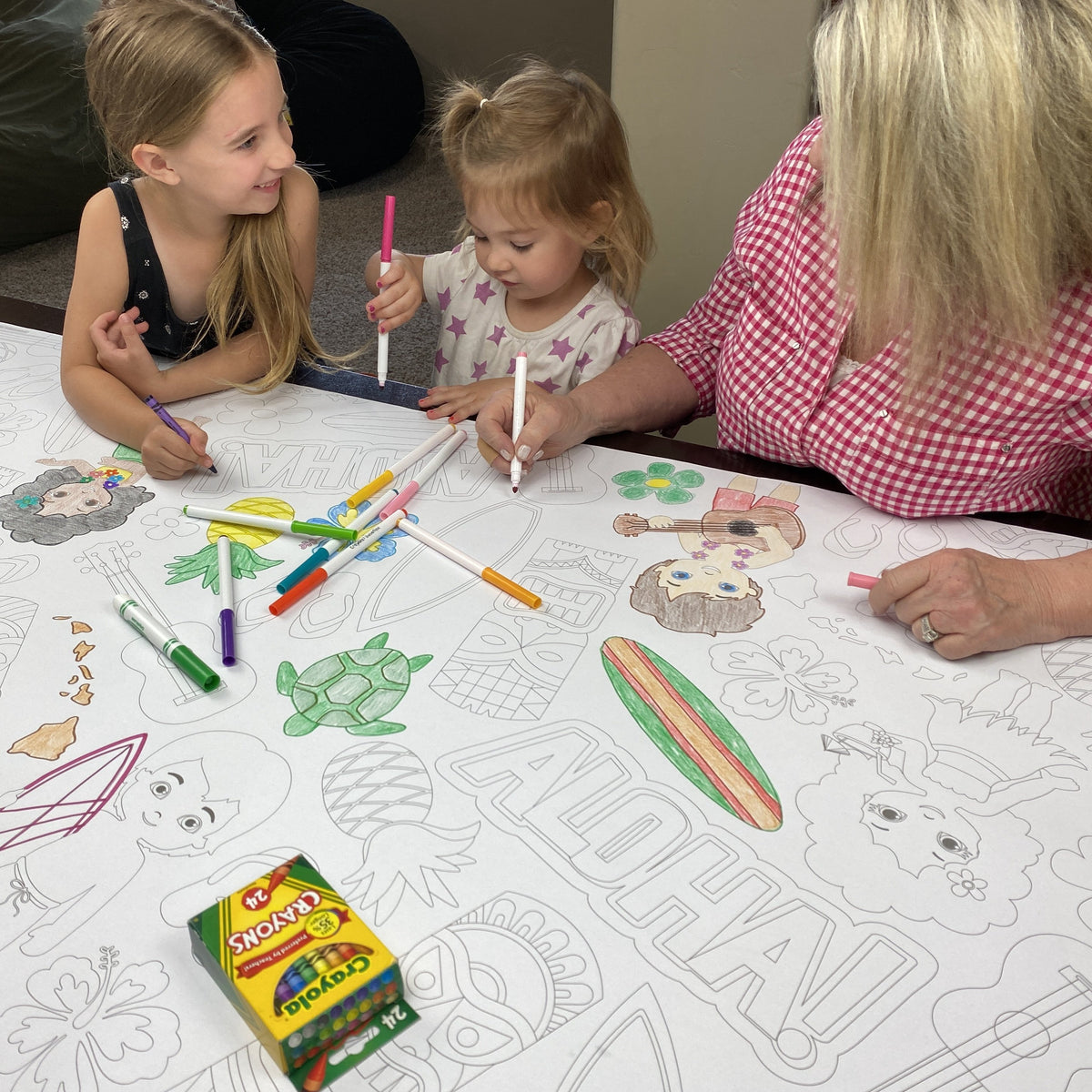 The Aloha giant coloring sheet being colored in with markers at a table