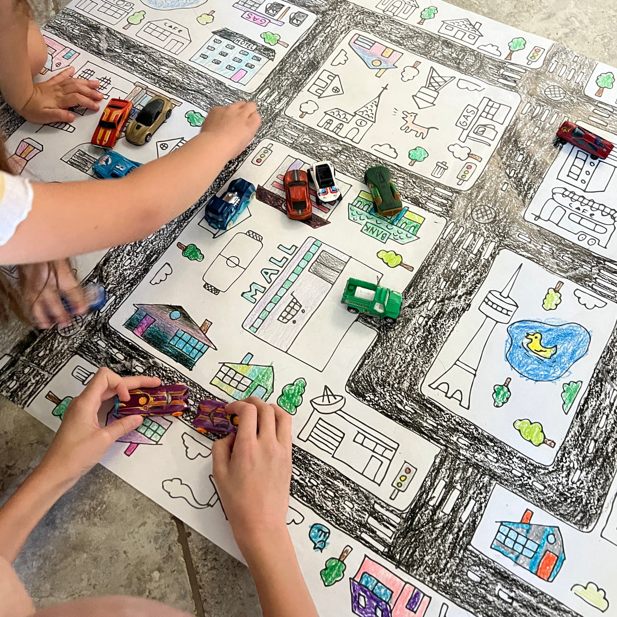 Kids playing with toy cars on the colored-in Around the Town giant coloring sheet