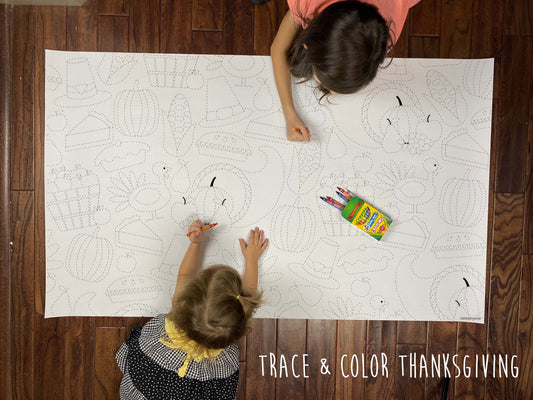 Child coloring the Thanksgiving Trace & Color giant coloring sheet on a wood floor with crayons